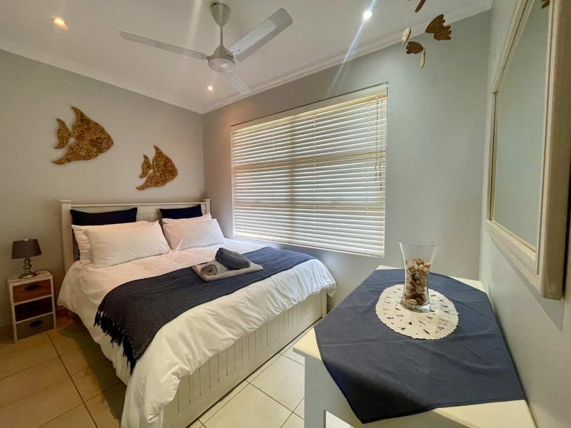 A well-maintained bedroom featuring tiled flooring, a ceiling fan, and venetian blinds, offering a comfortable and functional living space.
