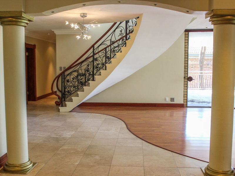 Spacious entrance hall featuring a grand curved staircase with wrought iron balustrade, elegant decorative columns, and a mix of stone and hardwood flooring.