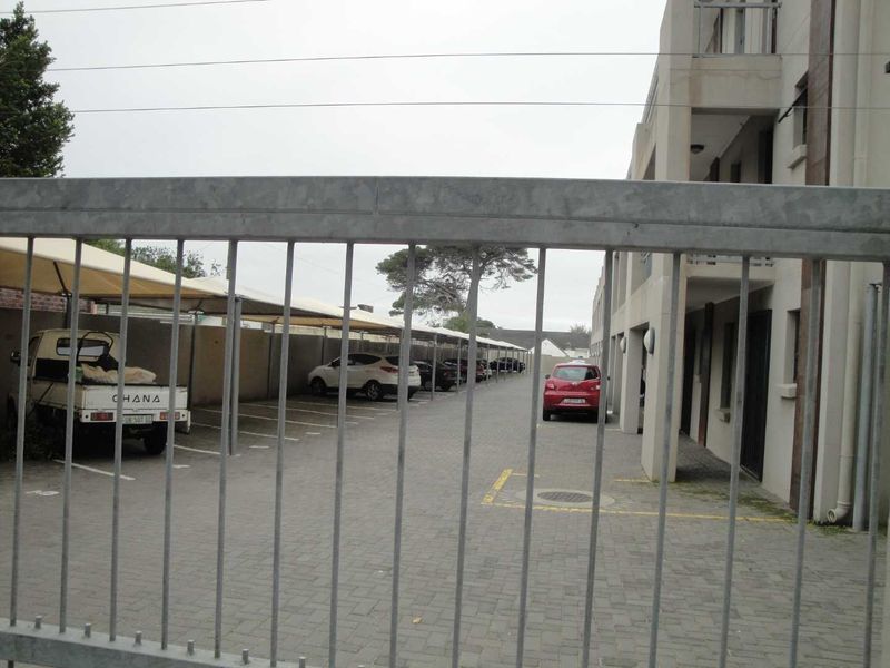View of the apartment complex parking area featuring paved driveway and covered carport bays, secured by a metal gate.