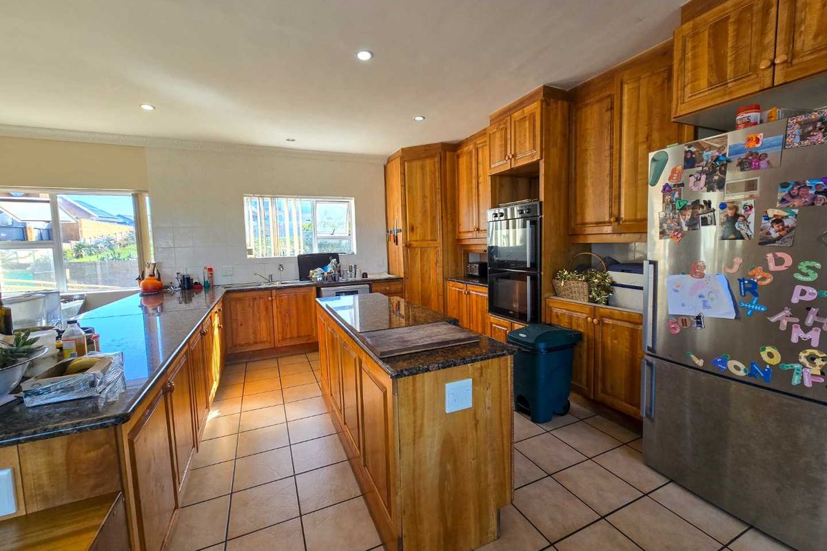 Spacious kitchen featuring timber cabinetry, granite countertops, a central island, and built-in double oven, offering ample storage and workspace.