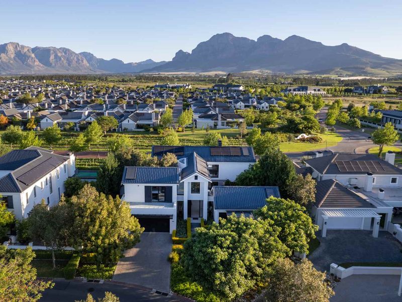 Aerial view of a modern residential property featuring a metal roof with solar panels, a paved driveway, and established garden in a scenic estate.
