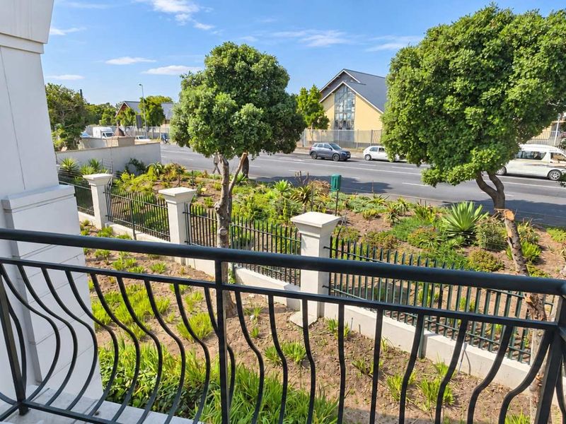 A clean, well-maintained balcony featuring a decorative wrought iron balustrade, overlooking a landscaped garden area and street frontage.