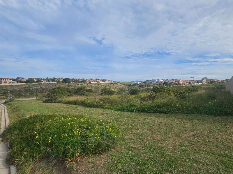 A wide-angle view of a vacant residential plot featuring natural grass landscaping and a paved verge, overlooking the surrounding neighborhood.