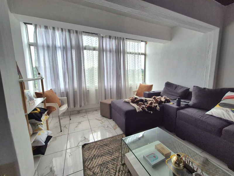 A bright living room featuring large windows that provide ample natural light and modern tiled flooring throughout the space.