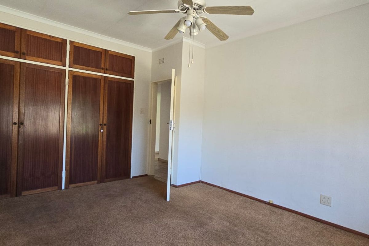 A bedroom featuring built-in wooden cupboards, carpeted flooring, and a ceiling fan.