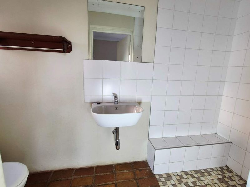 A functional bathroom featuring a wall-mounted basin, tiled splashback, and a built-in tiled shower bench with dated ceramic flooring.