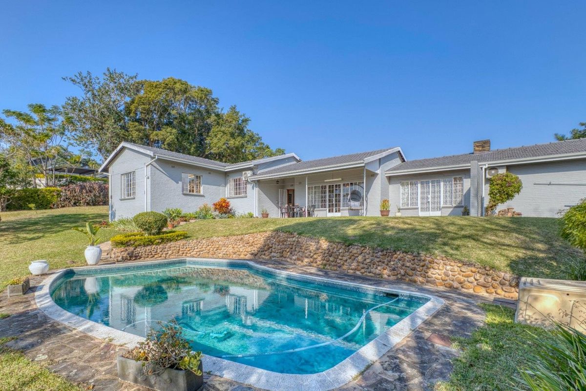 Rear view of the house featuring a swimming pool, stone retaining wall, covered patio area, and well-maintained garden.