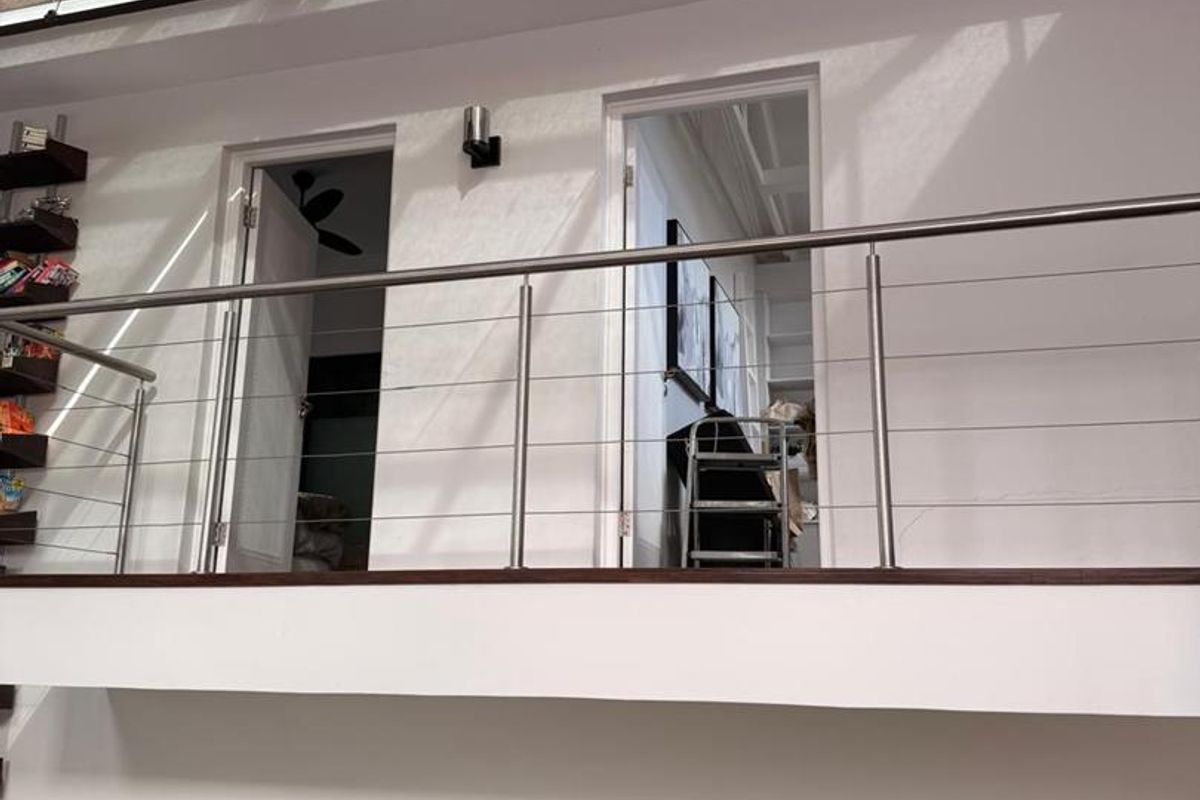 An open-plan living space featuring a mezzanine level with a stainless steel balustrade, a large skylight, and a modern kitchen with a central island.