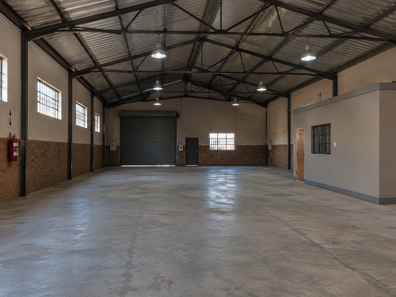 Spacious industrial utility space featuring high exposed steel trusses, concrete flooring, a large roller shutter door, and an integrated internal office partition.