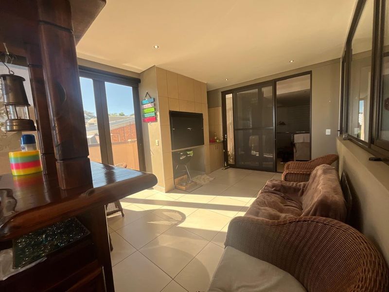 Covered patio area featuring a built-in braai, tiled flooring, and large sliding glass doors providing access to the outdoor space.