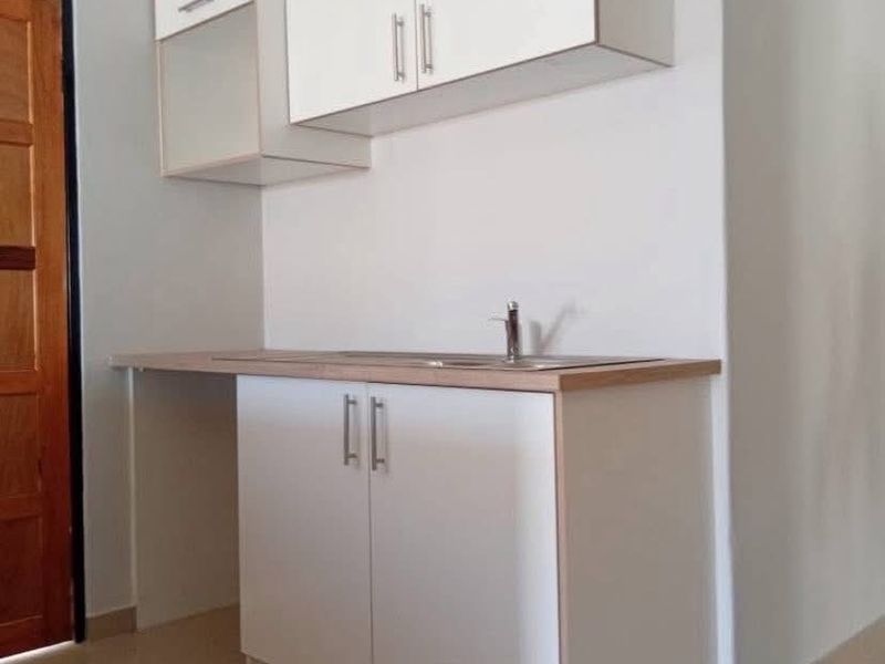 A compact kitchen area featuring white built-in cabinetry, a laminate countertop, and a stainless steel sink with tiled flooring.