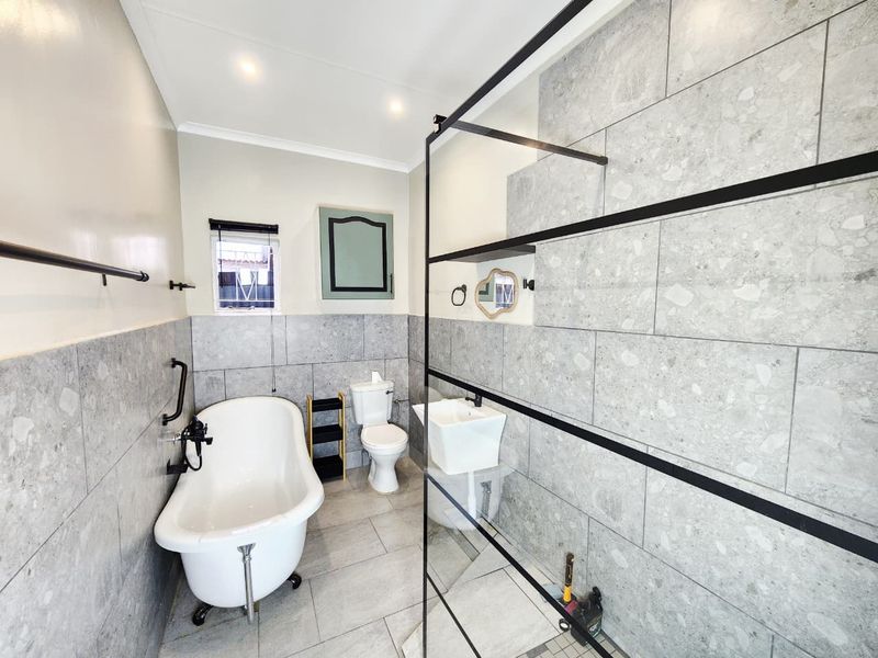 Modern bathroom featuring a freestanding bathtub, a walk-in shower with a black-framed glass screen, and contemporary grey stone-look tiling throughout.