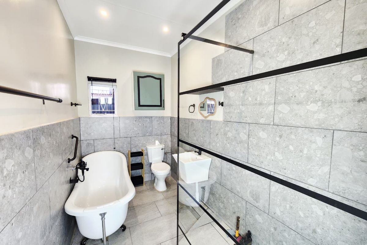 Modern bathroom featuring a freestanding bathtub, a walk-in shower with a black-framed glass screen, and contemporary grey stone-look tiling throughout.