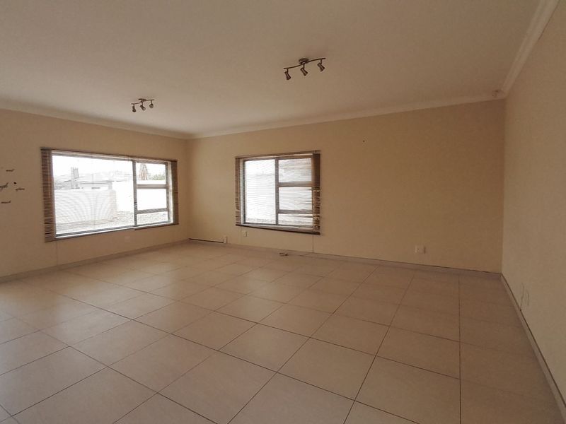 Spacious, empty living area featuring neutral tiled flooring, aluminium window frames, and modern track lighting, offering a blank canvas for interior design.