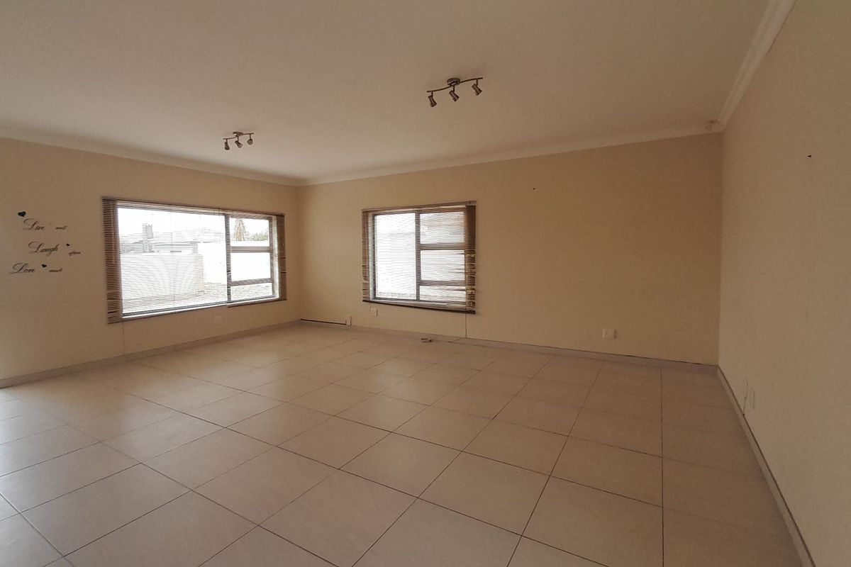 Spacious, empty living area featuring neutral tiled flooring, aluminium window frames, and modern track lighting, offering a blank canvas for interior design.