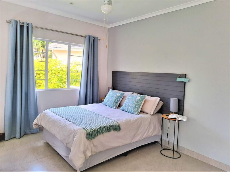 A bright and well-maintained bedroom featuring tiled flooring, a ceiling fan, and a large window allowing for natural light.