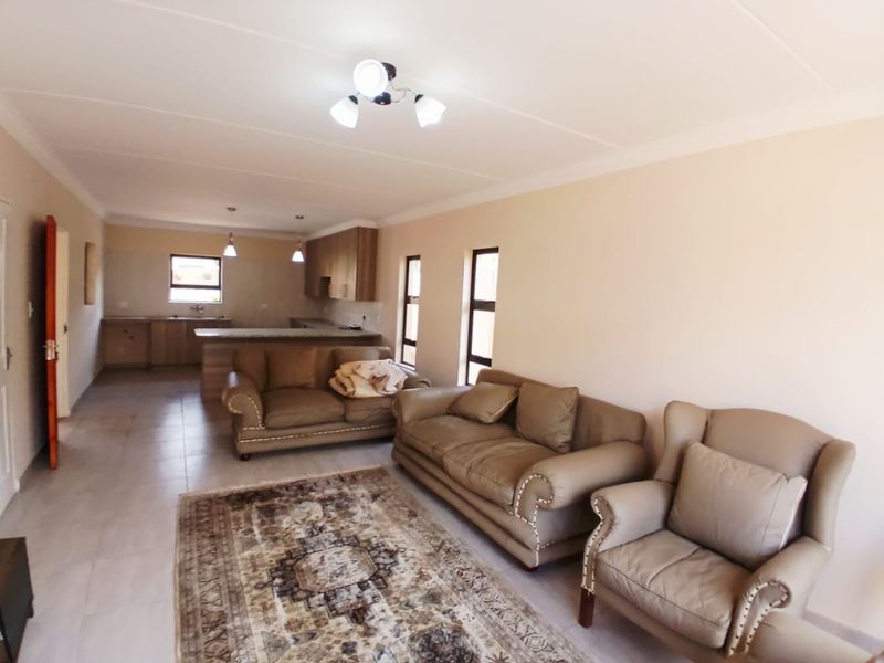 An open-plan living and kitchen area featuring tiled floors, neutral walls, and built-in kitchen cabinetry with a breakfast island.