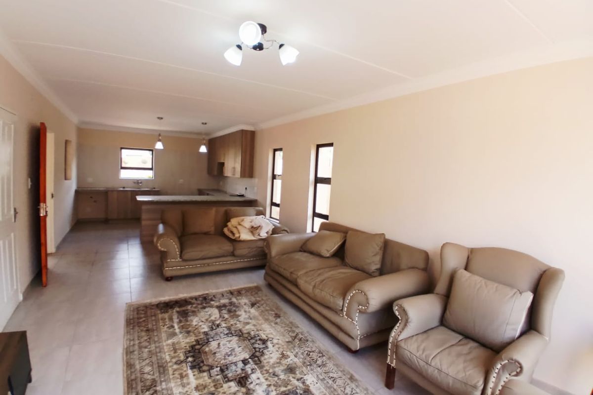 An open-plan living and kitchen area featuring tiled floors, neutral walls, and built-in kitchen cabinetry with a breakfast island.