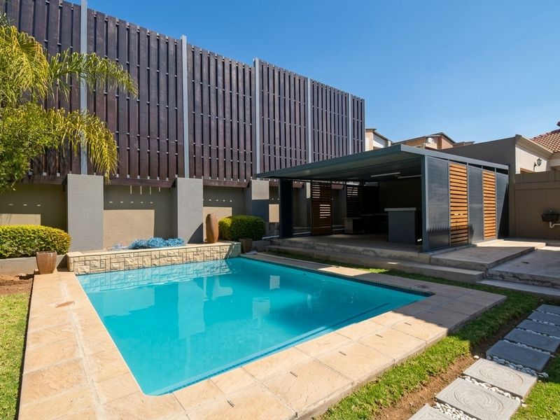 Outdoor entertainment area featuring a swimming pool with stone coping, adjacent covered patio, and timber privacy screening in a well-maintained garden setting.