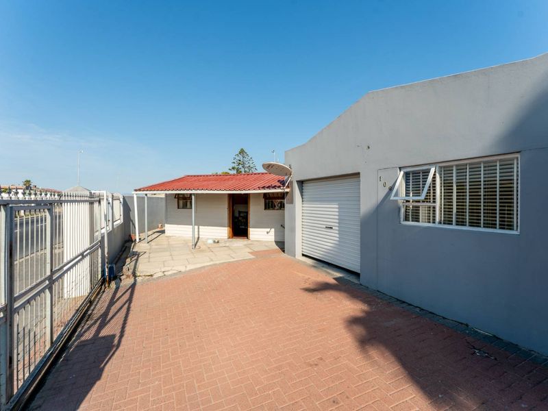 Front exterior view featuring a paved driveway, single garage, and a covered patio area with secure metal gate access.