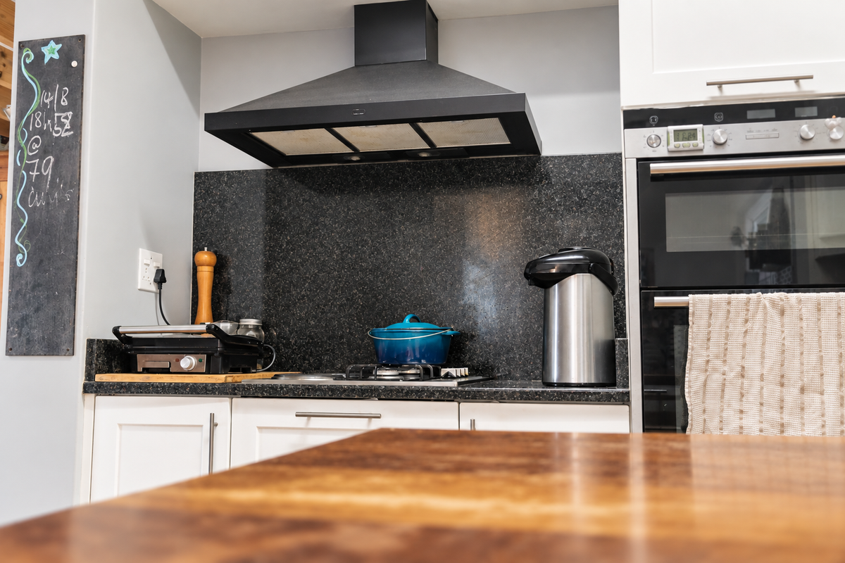 A well-maintained kitchen area featuring a built-in oven, gas hob, black granite splashback, and modern shaker-style cabinetry.