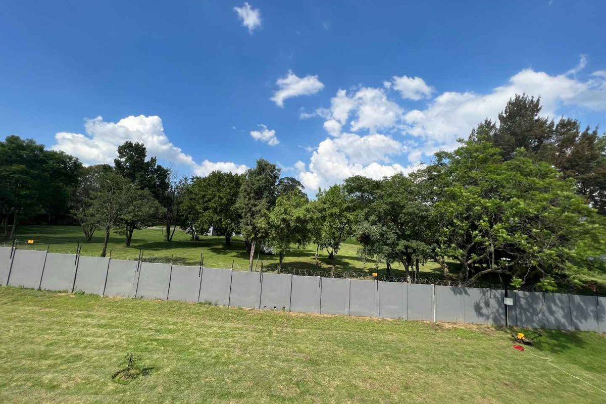 A view of the rear garden area featuring a lawn and a perimeter precast concrete wall topped with razor wire.