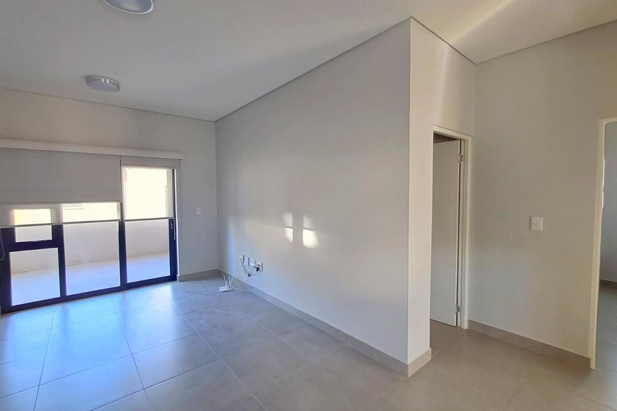 A bright, empty living area featuring neutral tiled flooring, modern ceiling lighting, and a sliding glass door providing access to an outdoor balcony.