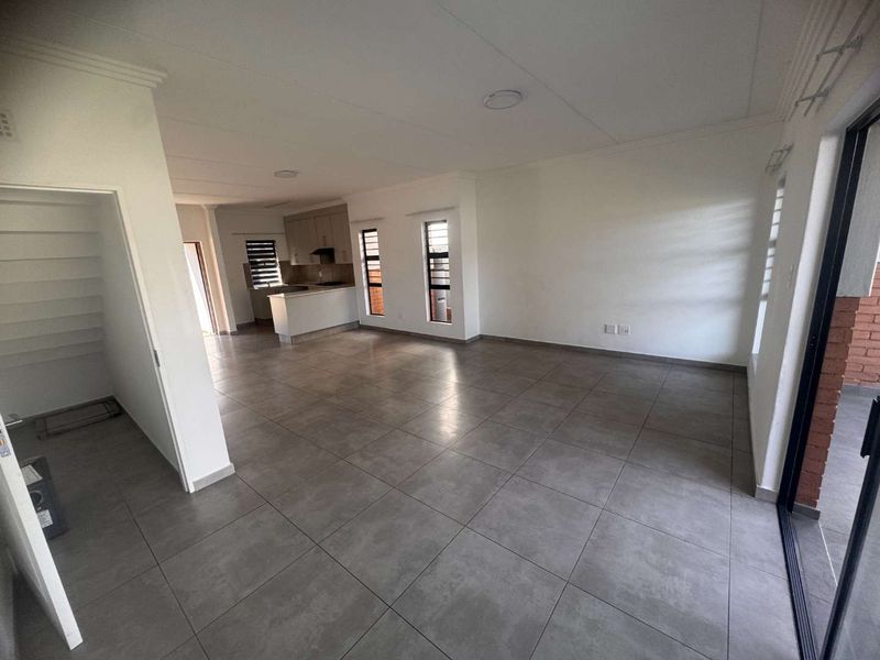 Spacious open-plan living area featuring large format floor tiles, neutral walls, and a modern kitchen with built-in cabinetry and a breakfast peninsula.