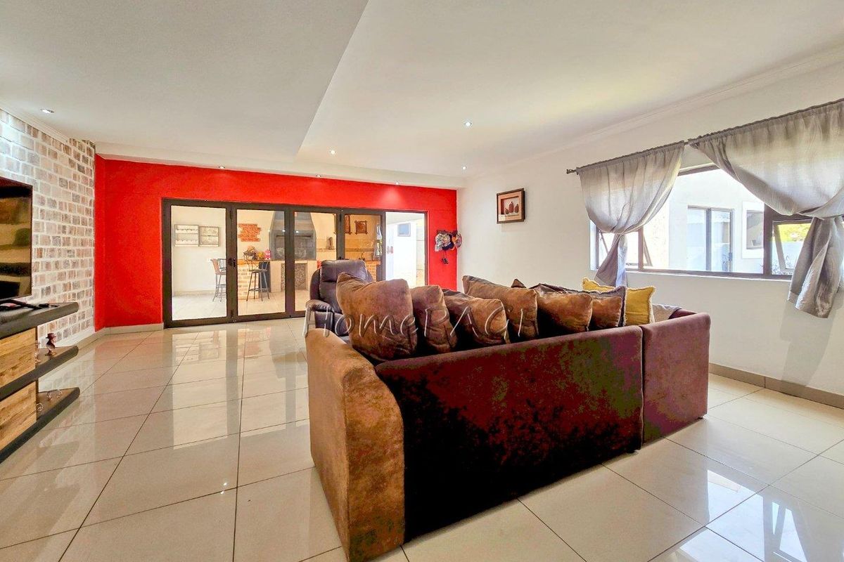 Spacious living area featuring large format floor tiles, a striking red accent wall, and folding glass doors leading to an outdoor patio space.