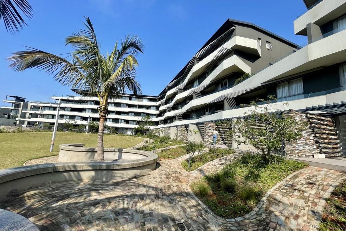 Modern apartment complex exterior featuring contemporary architecture, stone-paved pathways, landscaped garden areas, and private balconies with glass balustrades.