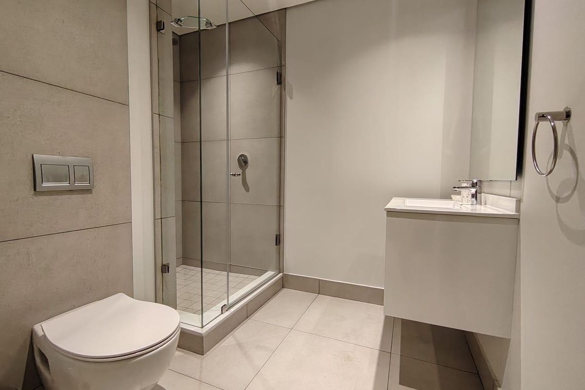 Modern bathroom featuring a floating vanity, wall-mounted toilet, and a glass-enclosed shower with neutral large-format tiling.
