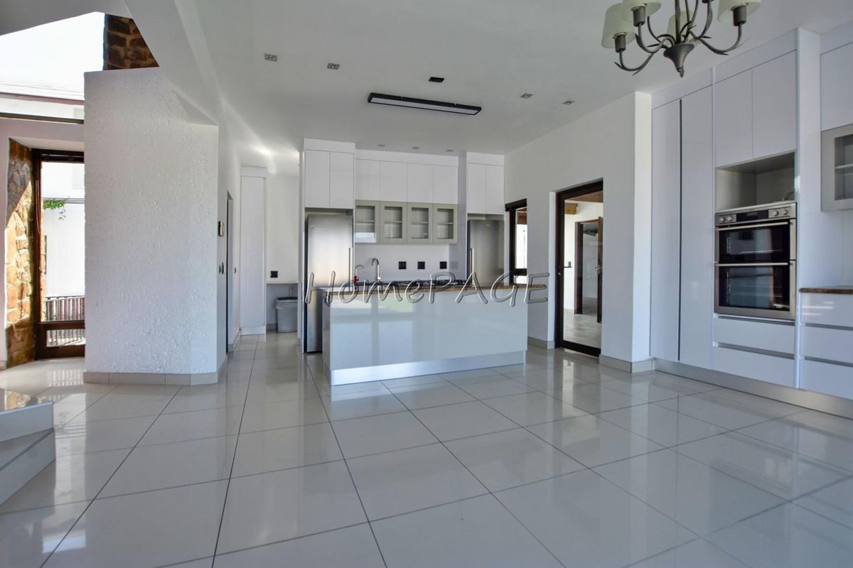 Modern open-plan kitchen featuring sleek white cabinetry, integrated double ovens, a central island, and polished floor tiles.