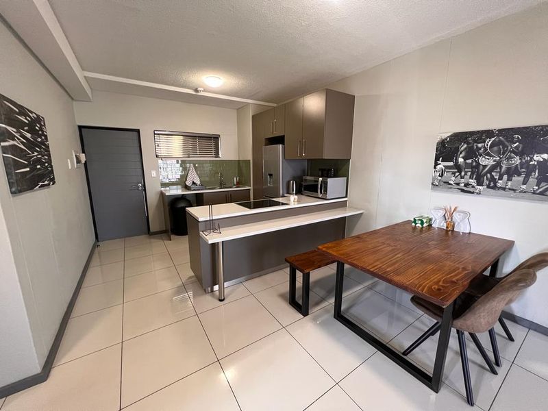 An open-plan kitchen and dining area featuring modern cabinetry, a functional kitchen island with a hob, and neutral tiled flooring throughout.