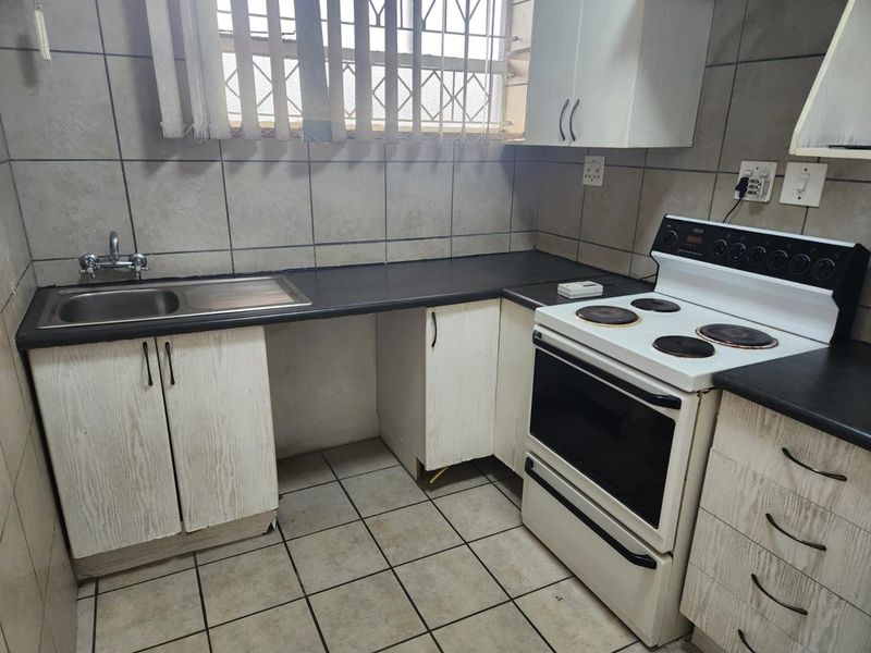 A functional kitchen featuring built-in cabinetry, a stainless steel sink, and a freestanding stove, with tiled finishes throughout.
