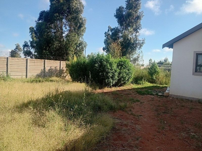 Rear exterior view of the property featuring a large, unmaintained garden area enclosed by a precast concrete boundary wall with security razor wire.