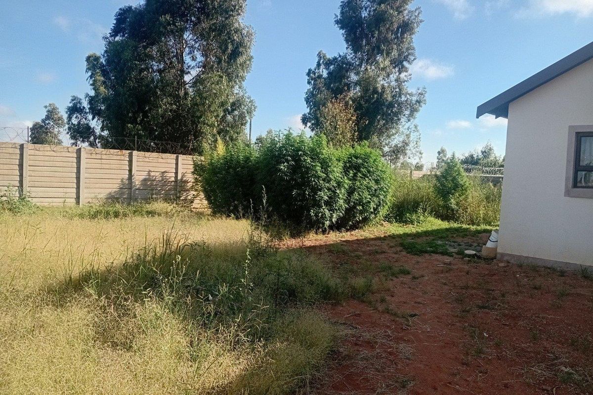 Rear exterior view of the property featuring a large, unmaintained garden area enclosed by a precast concrete boundary wall with security razor wire.