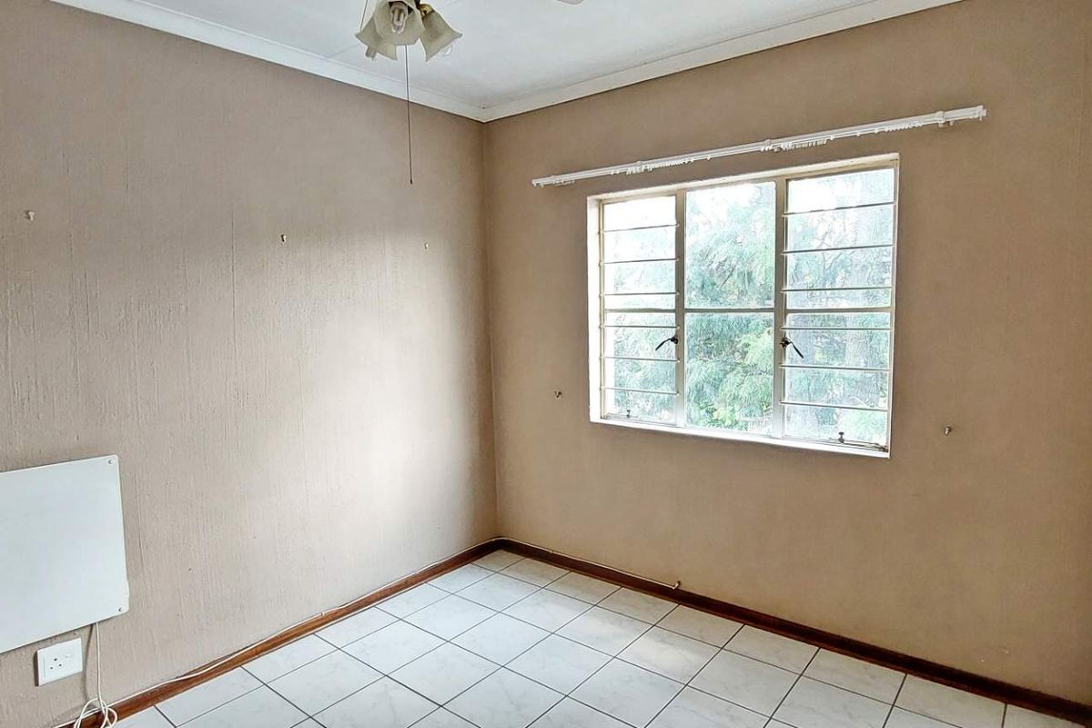 An empty bedroom featuring tiled flooring, a wall-mounted heater, and a window with security bars.