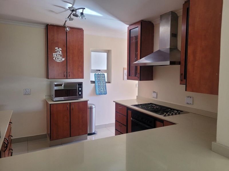 A functional kitchen featuring wooden cabinetry, stone countertops, a gas hob, and a stainless steel extractor fan.