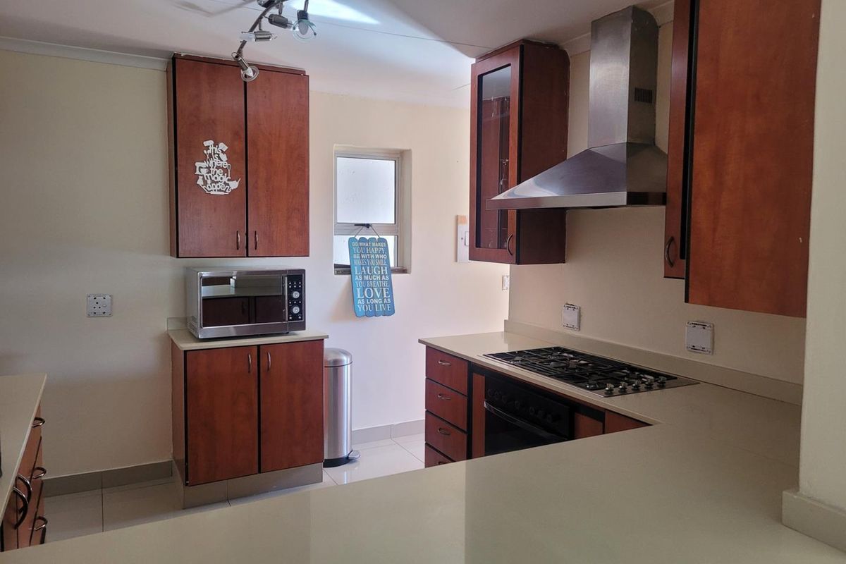A functional kitchen featuring wooden cabinetry, stone countertops, a gas hob, and a stainless steel extractor fan.