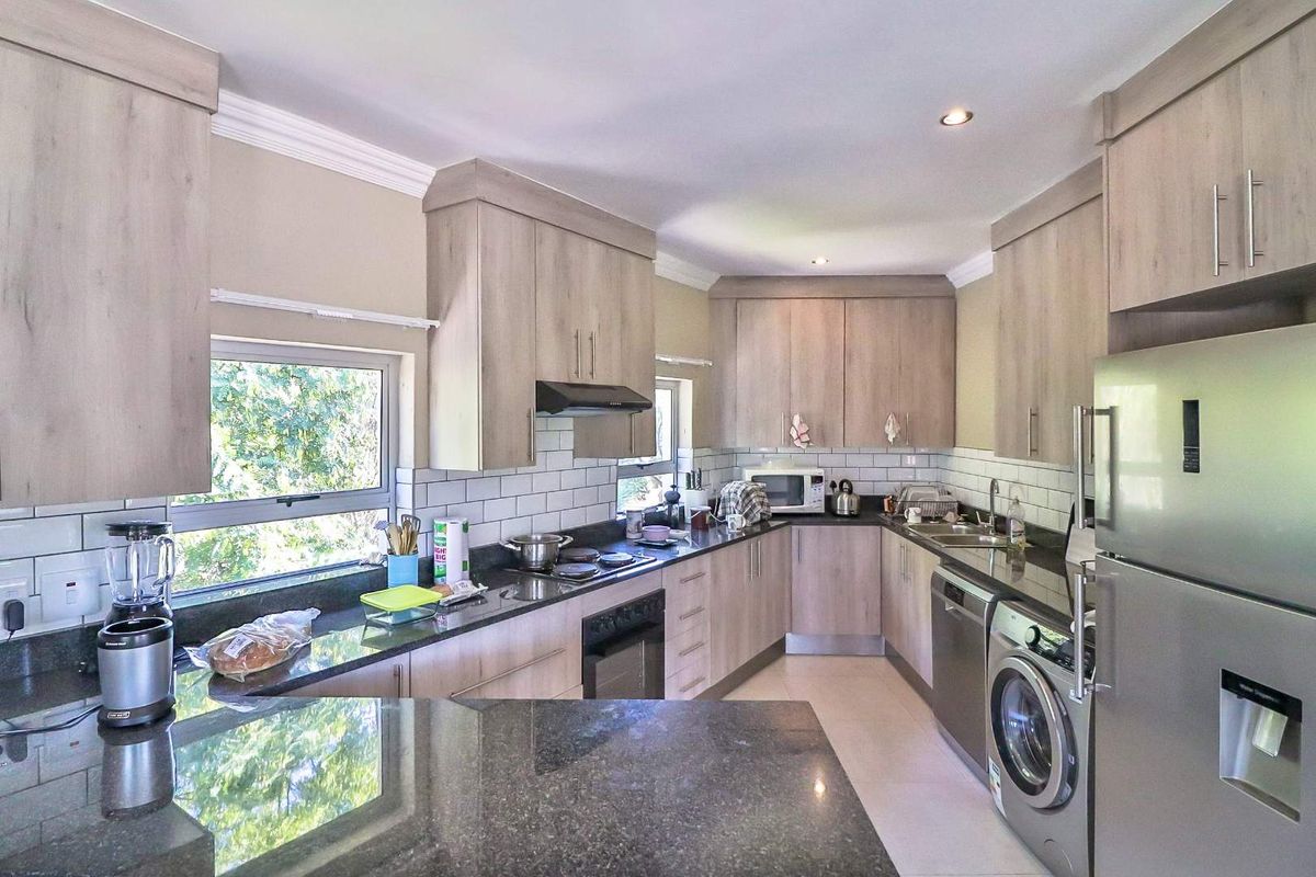 A functional kitchen featuring light wood-toned cabinetry, dark granite countertops, subway tile backsplash, and integrated space for laundry appliances.