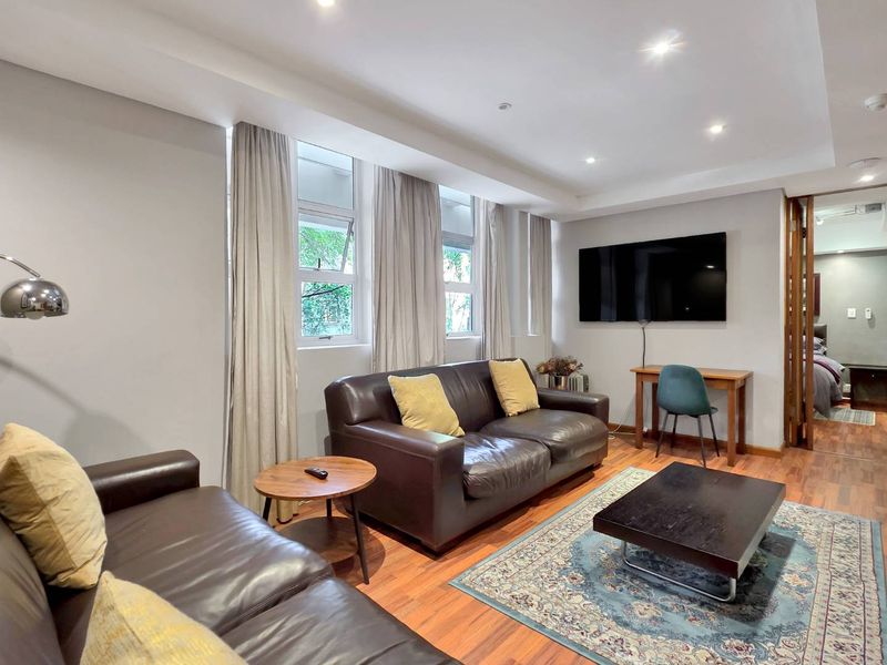 A well-maintained living room featuring timber flooring, recessed downlighting, and large windows that provide natural light.