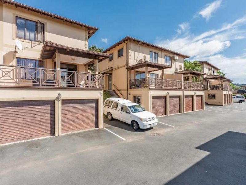 Exterior view of a townhouse complex featuring multiple garage units, private balconies with metal railings, and a paved driveway area.