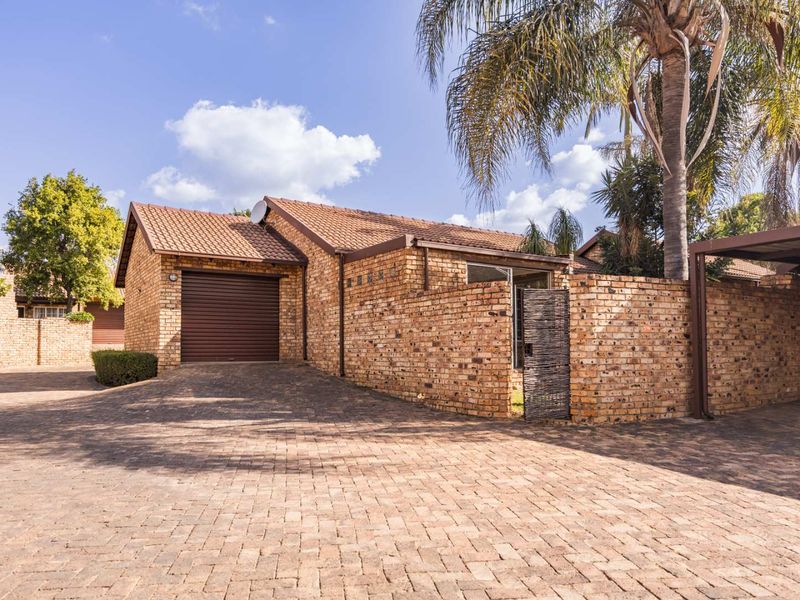 Front exterior view of a face brick townhouse featuring a paved driveway, single garage, and an attached carport.
