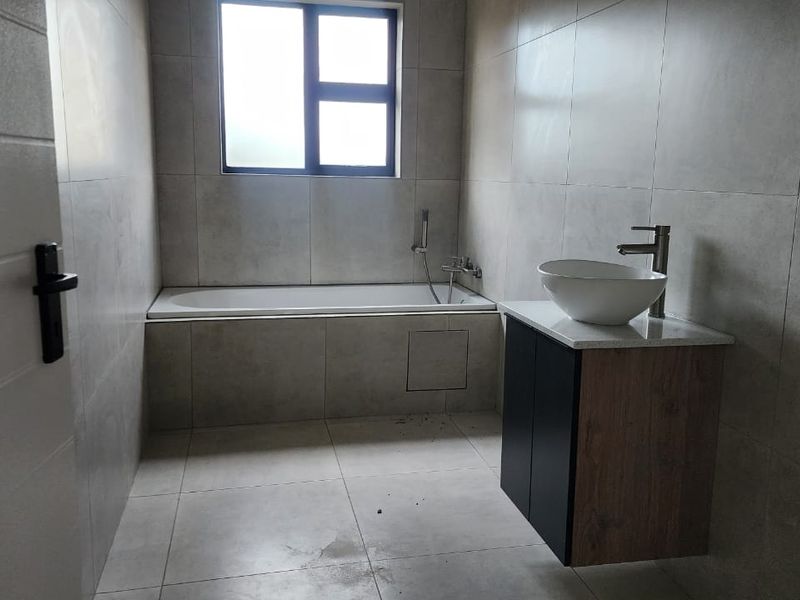 A modern, minimalist bathroom featuring large-format wall and floor tiles, a built-in bathtub, and a contemporary wall-mounted vanity with a vessel sink.