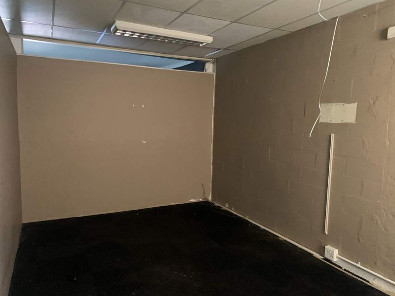 An empty office space featuring a suspended ceiling, carpeted flooring, and exposed brick walls with visible electrical wiring.