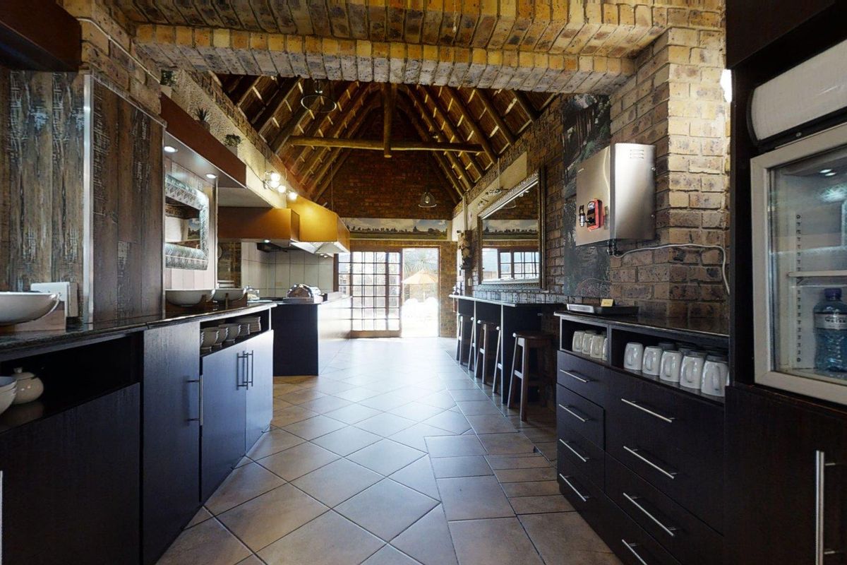 A rustic kitchen area featuring exposed brick walls, a high vaulted thatched ceiling, tiled flooring, and built-in cabinetry with integrated serving counters.