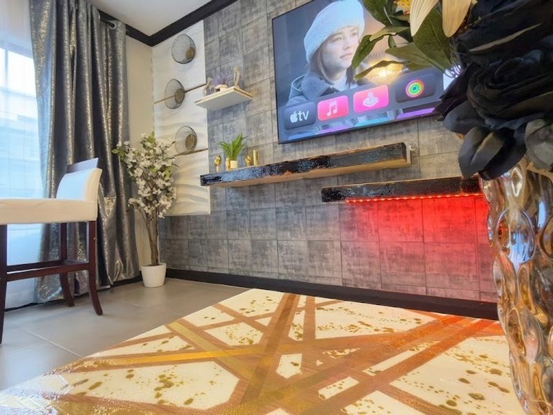 A modern living area featuring a textured feature wall with floating shelves, integrated LED lighting, and neutral tiled flooring.
