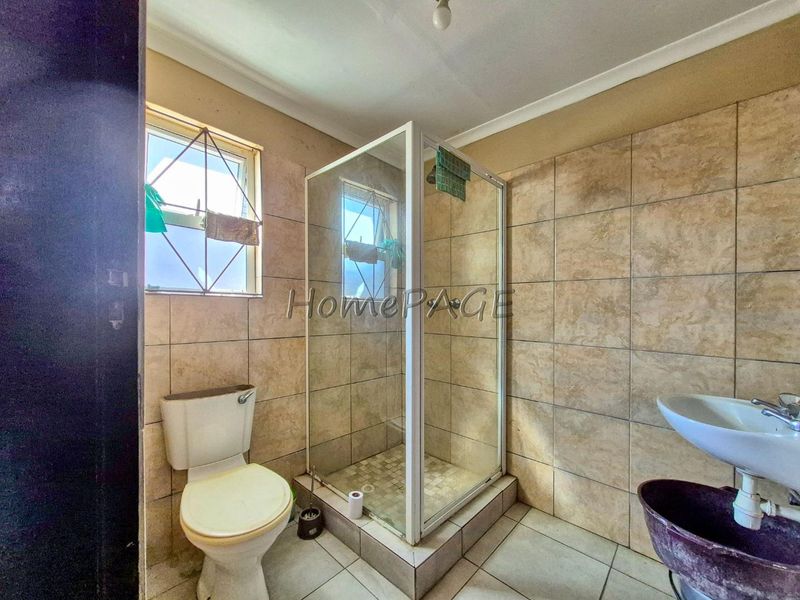 A functional bathroom featuring a shower enclosure, pedestal basin, and toilet, finished with neutral wall and floor tiles.