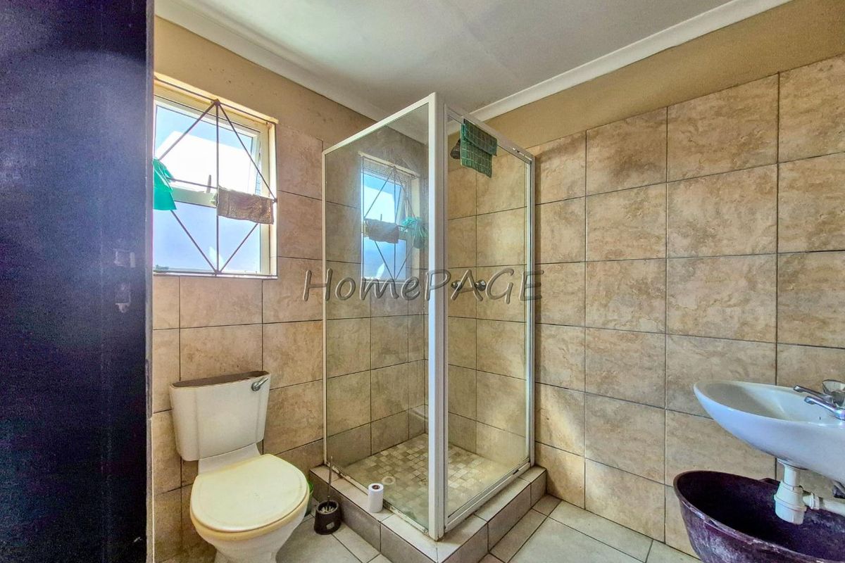A functional bathroom featuring a shower enclosure, pedestal basin, and toilet, finished with neutral wall and floor tiles.
