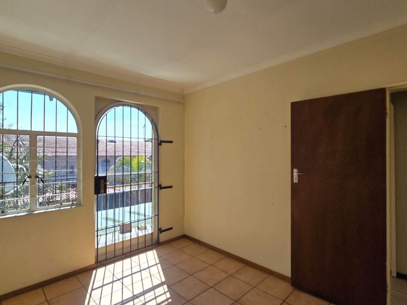 An empty living area featuring tiled flooring, arched windows with security bars, and a solid internal door.